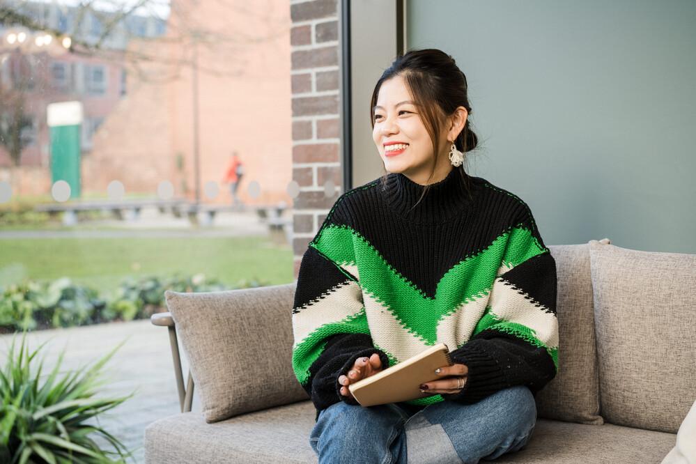 A student is looking left out of a window on a dry day. There is grass outside and she's wearing a green, white and black top.